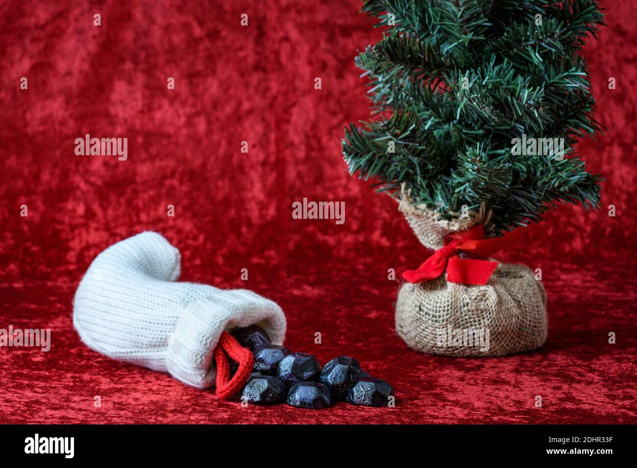 Calza di Natale che spillano fuori caramella di carbone, per i ragazzi e le ragazze cattivi, con un albero artificiale della sfera di burlap, su uno sfondo rosso Foto Stock