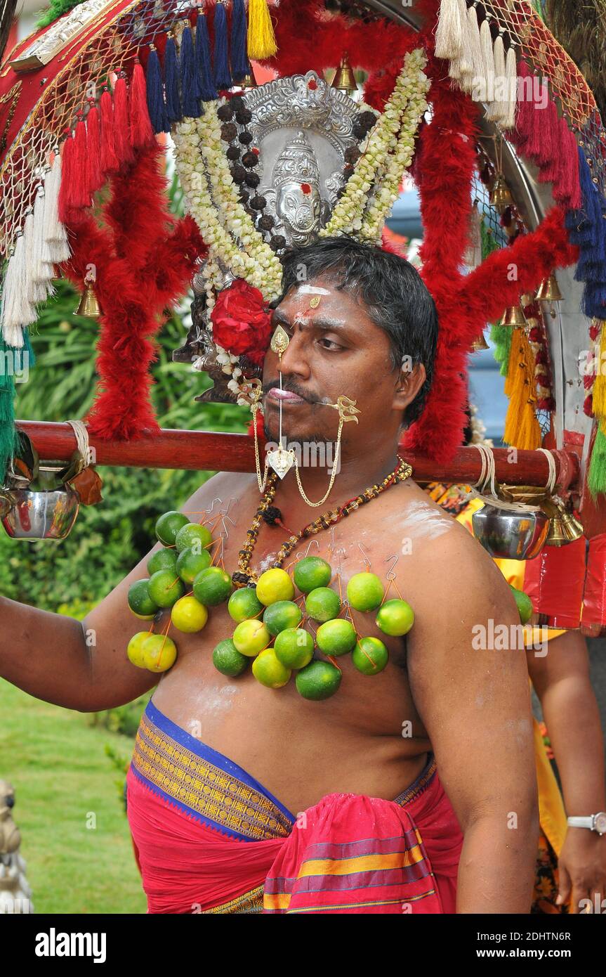 Un partecipante etnico tamil alla processione annuale di Thaipusam (Hindu) a Singapore, con la lingua trafitto e limoni attaccati tramite uncini sul suo corpo Foto Stock