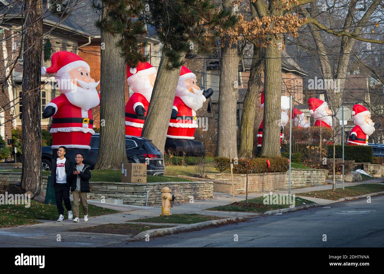 Toronto, Canada. 11 Dicembre 2020. La gente cammina oltre le clausole gonfiabili giganti di Santa su Inglewood Drive a Toronto, Canada, 11 dicembre 2020. A partire dal 2013, decine di clausole di Santa gonfiabili alte 14 piedi si estendono lungo Inglewood Drive a Toronto durante la stagione delle vacanze, attirando molti visitatori. Credit: Zou Zheng/Xinhua/Alamy Live News Foto Stock