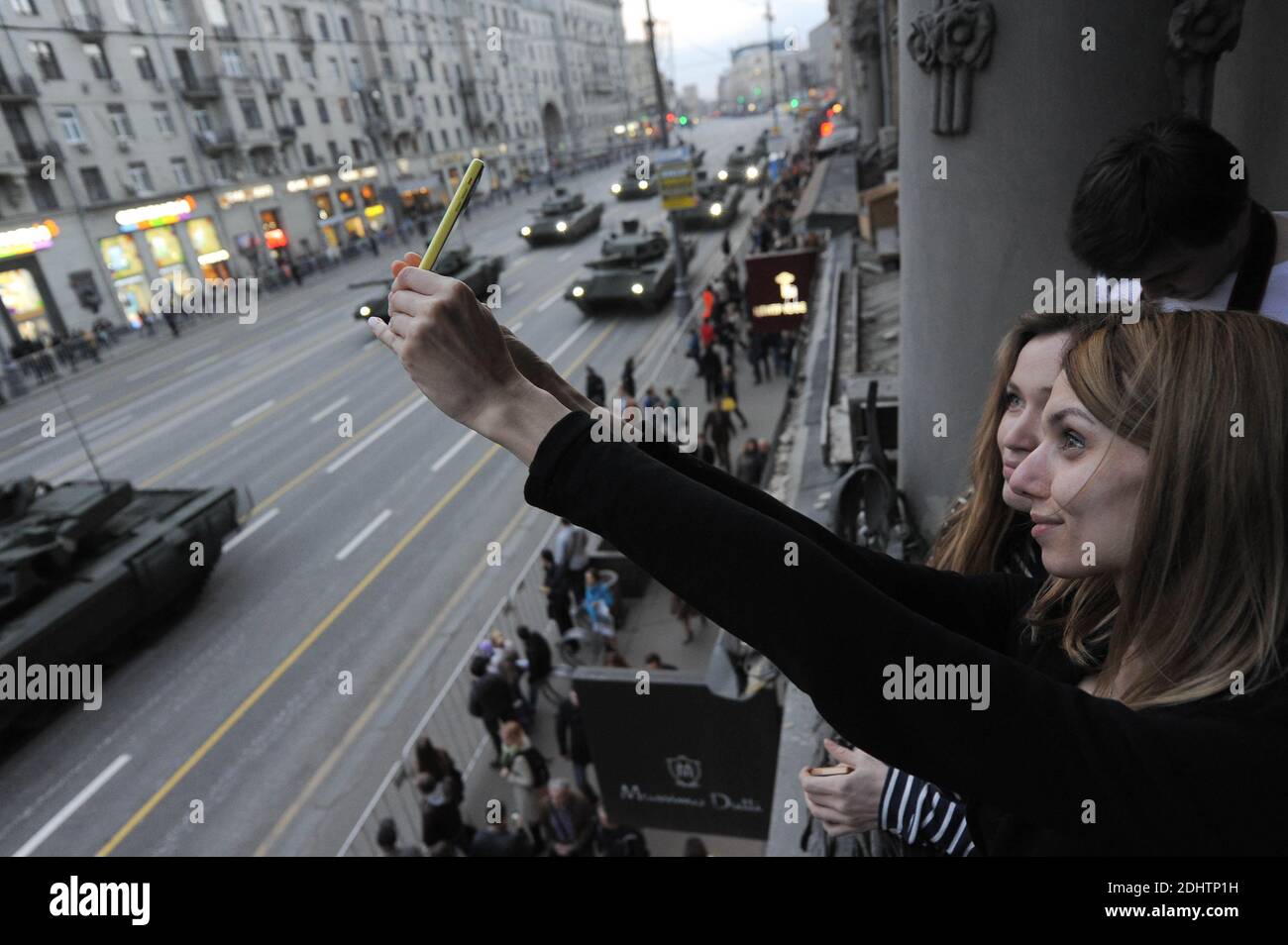 Le ragazze prendono un selfie contro lo sfondo di equipaggiamento militare.equipaggiamento militare su Tverskaya Street prima di muoversi verso la Piazza Rossa per una prova per la parata della Festa della Vittoria nel centro di Mosca. Foto Stock