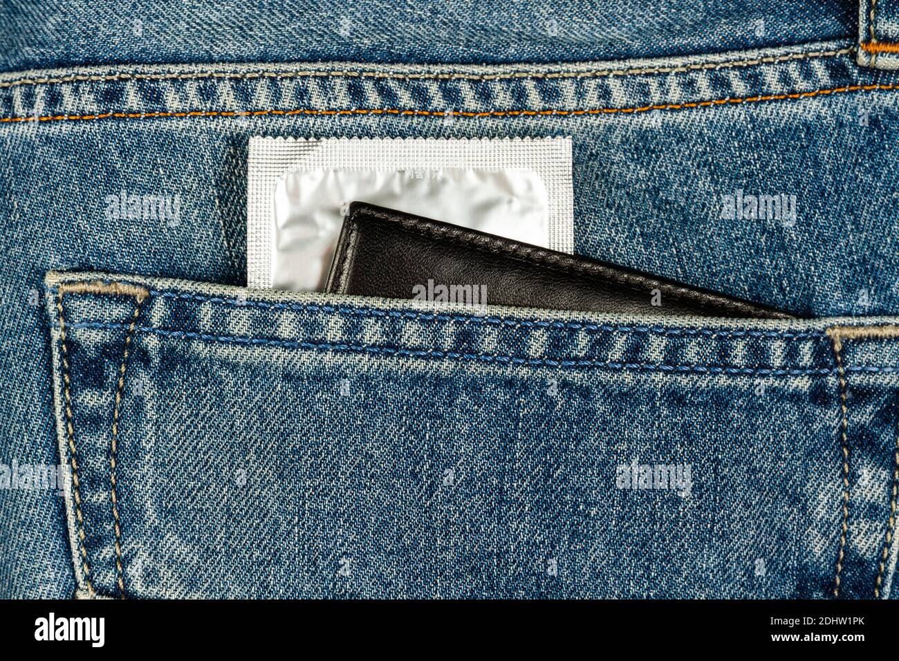 un preservativo in una confezione d'argento e un portafoglio che si attacca da una tasca per i jeans Foto Stock