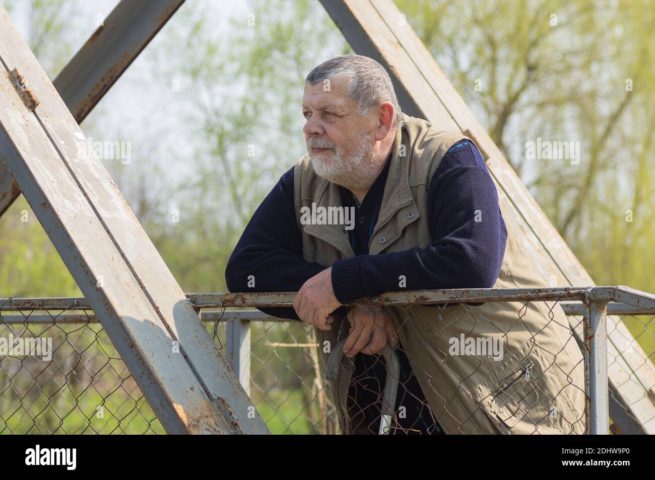 Ritratto dell'uomo caucasico con bastone in piedi un ponte pedonale in metallo e guardando la distanza Foto Stock