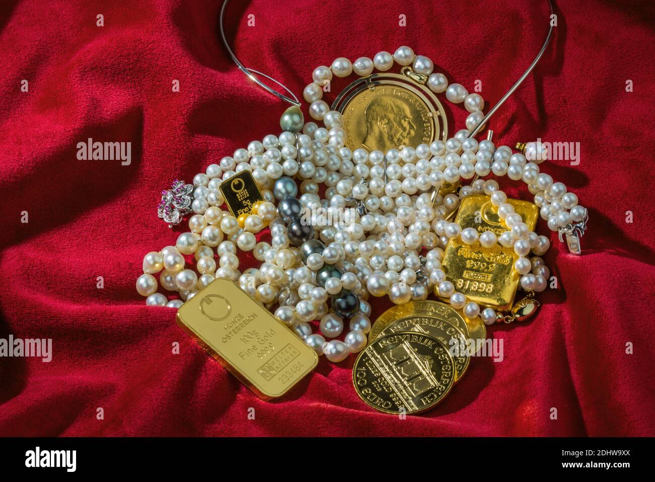 Oro in Münzen und sterile mit Schmuck auf rotem Samt. Symbolfoto für Reichtum, Luxus, Reichensteuer. Foto Stock