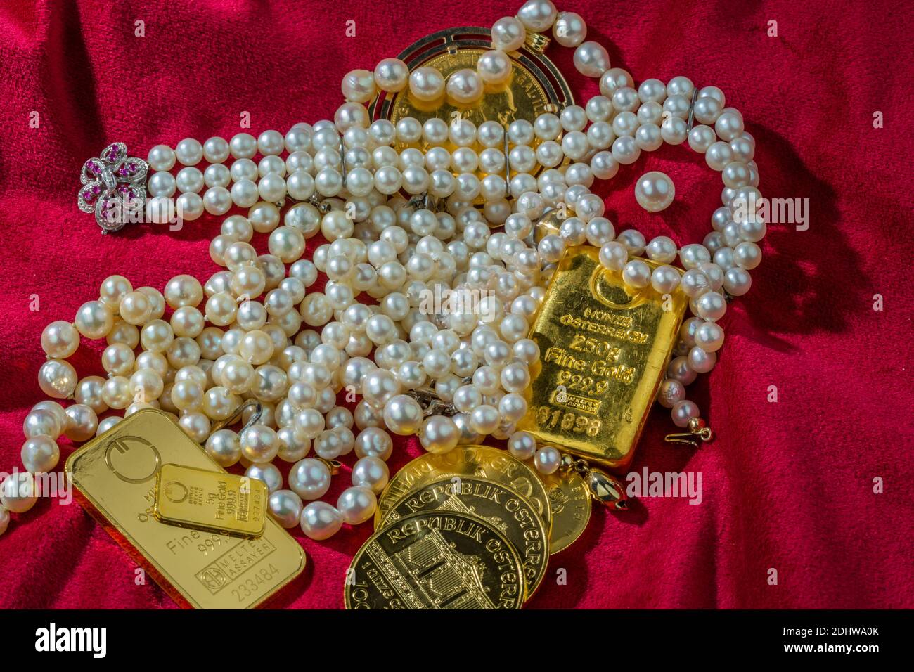 Oro in Münzen und sterile mit Schmuck auf rotem Samt. Symbolfoto für Reichtum, Luxus, Reichensteuer. Foto Stock