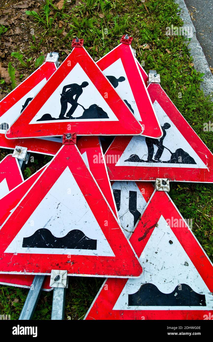 Viele Verkehrszeichen einer Strassenbaustelle liegen übereinander am Boden. Foto Stock