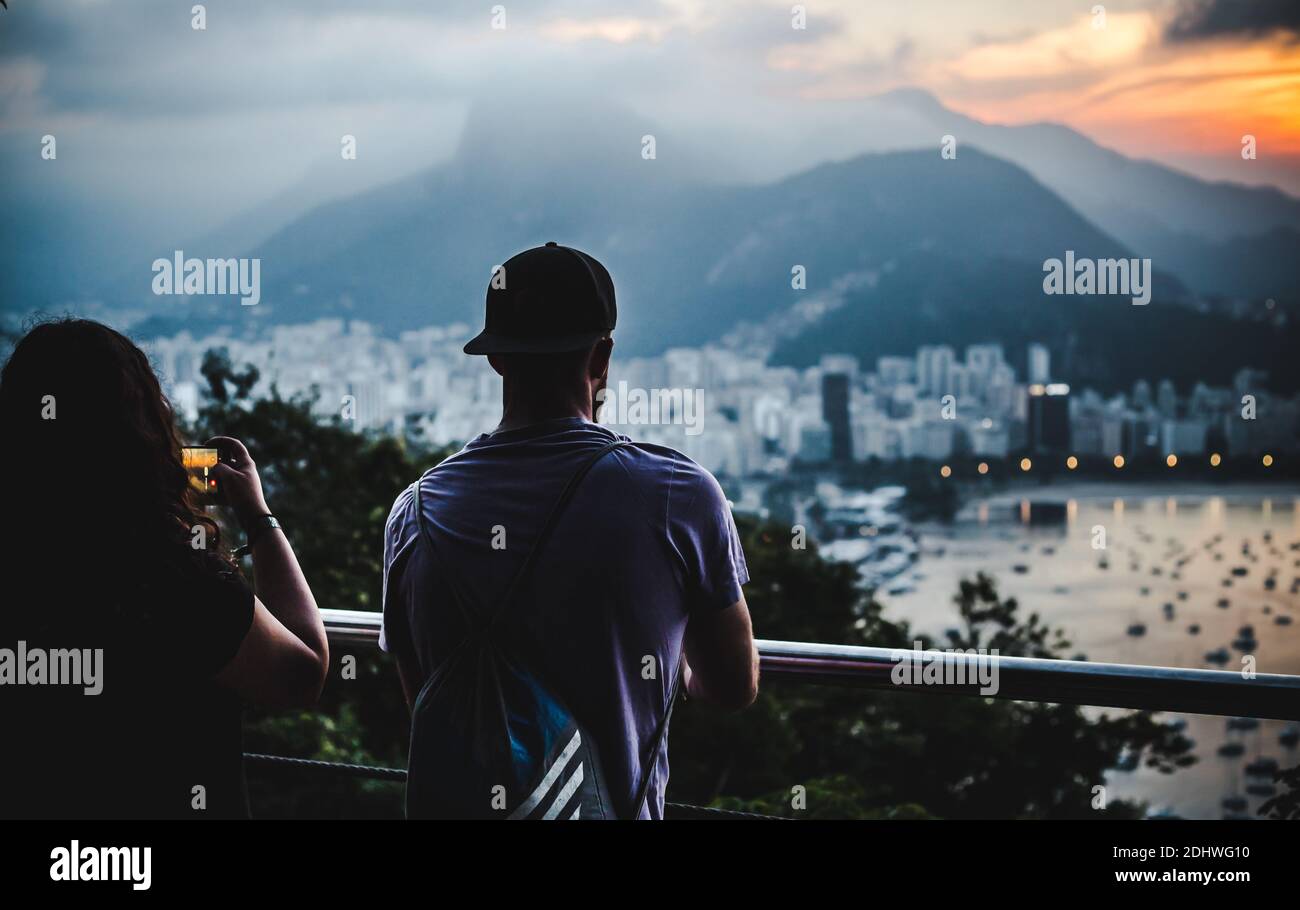 I turisti in viaggio indietro scattano foto e guardano il tramonto sulle baie di Rio de Janeiro, Brasile, dalla cima del Pan di zucchero / Pão de Açucar Foto Stock