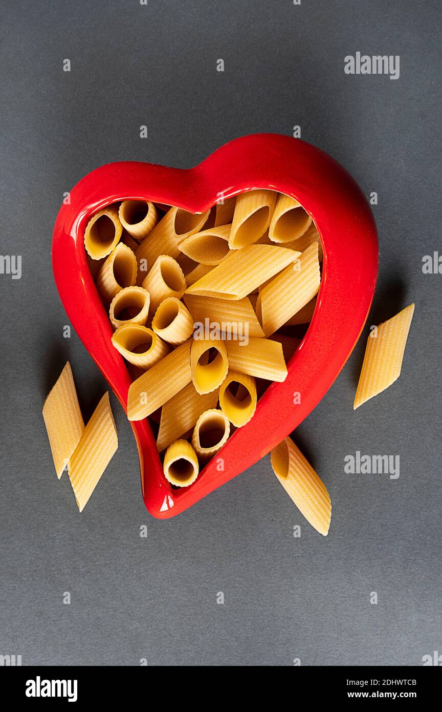 pasta fresca penne rigata in un contenitore a forma di cuore rosso su  sfondo grigio. vista zenith Foto stock - Alamy
