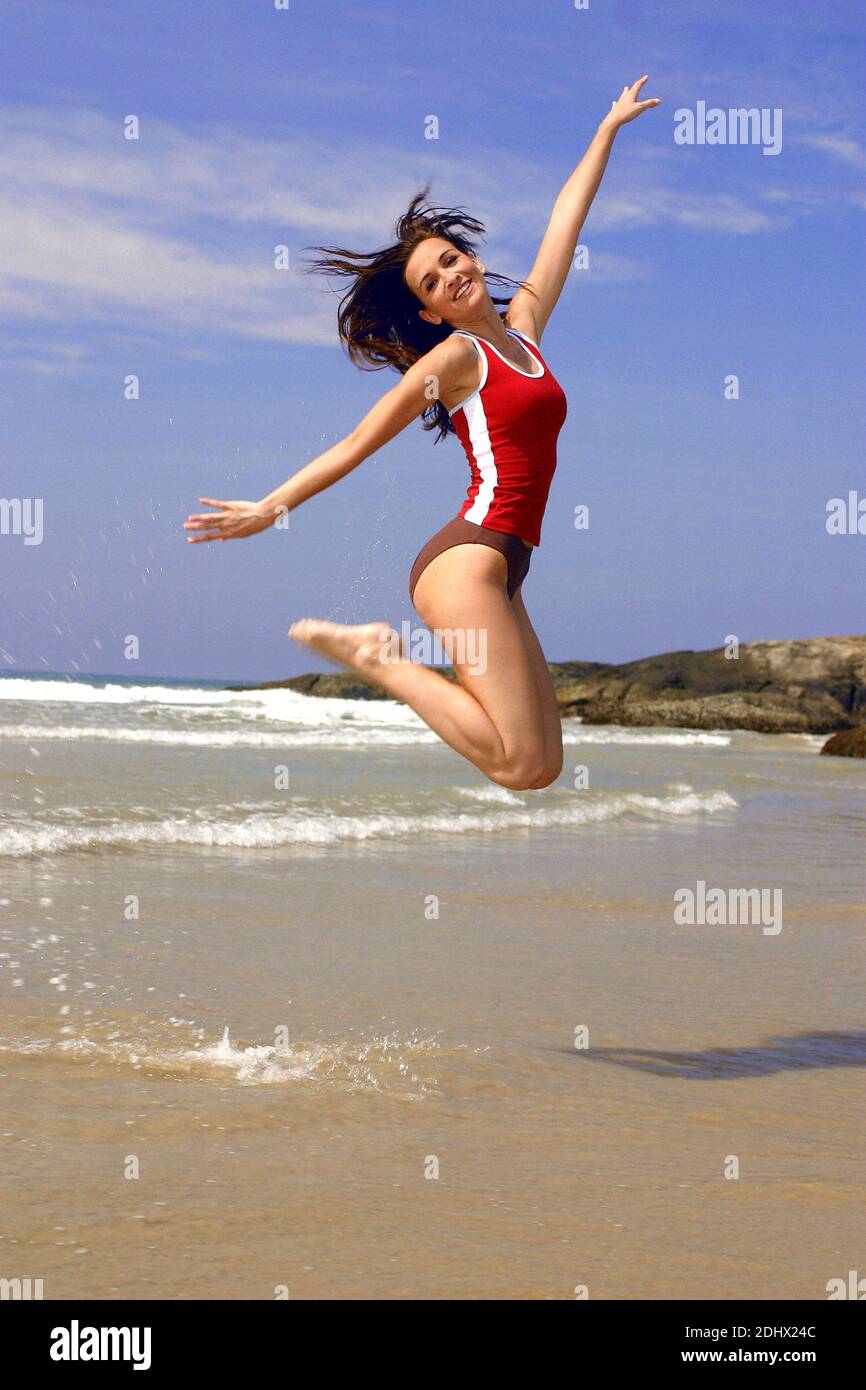 Junge Frau am Meer springt vor Freude in die Luft, endlich Urlaub, MR: Sì Foto Stock