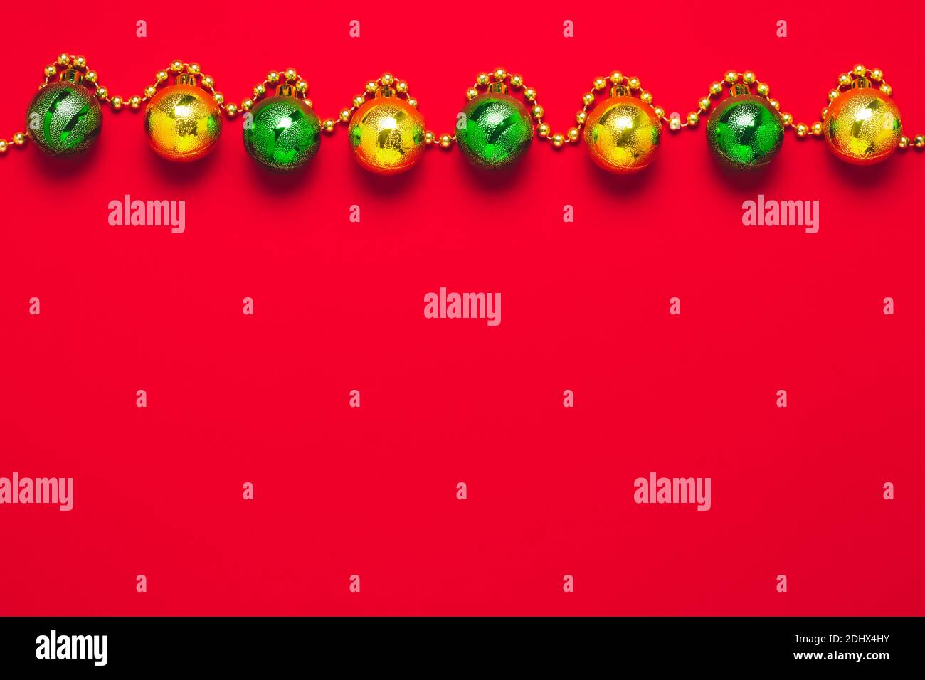 Sfondo rosso festivo con palline d'oro e verdi. Copiare lo spazio sulla carta regalo per le festività. Decorazioni invernali su modello natalizio, design minimalista e luminoso Foto Stock