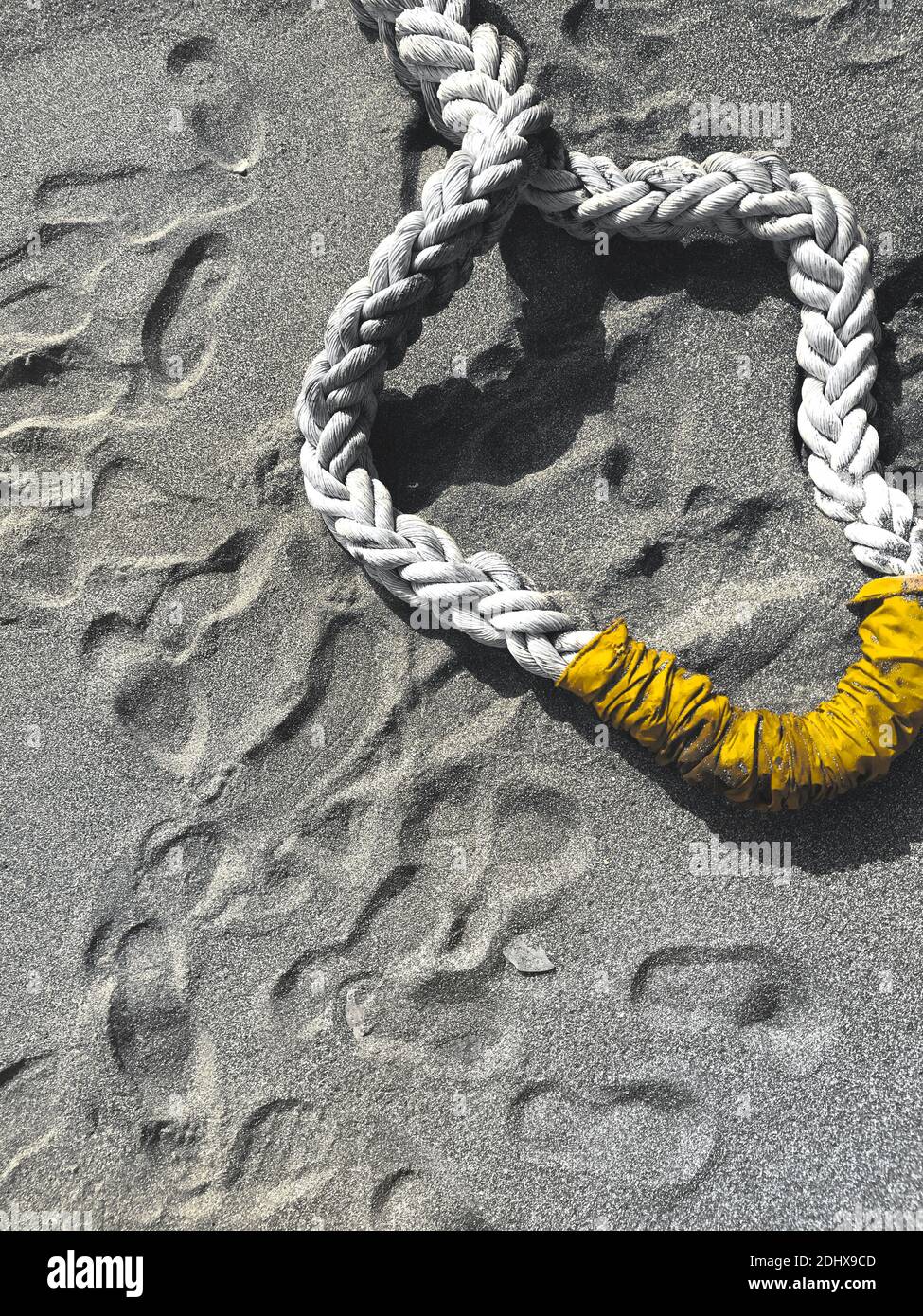 Spiaggia di sabbia grigia con corda di nave di colore giallo e impronte a terra. Sfondo astratto per l'illustrazione del concetto marino con spazio di testo Foto Stock