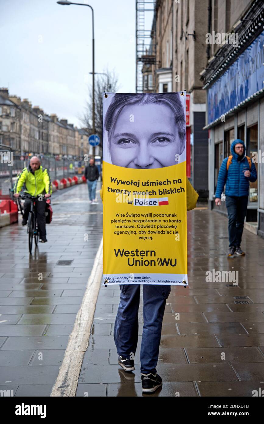 Uomo con un annuncio Western Union in polacco sulla sua schiena che cammina su Leith Walk a Edimburgo, Scozia, Regno Unito. Foto Stock