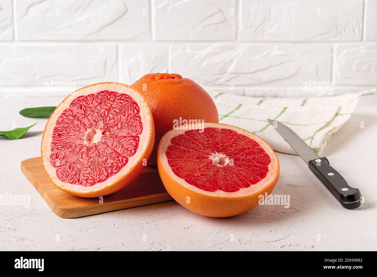 Pompelmo maturo intero e due succose metà su un tagliere e coltello. Ingrediente per dolci di frutta. Cibo vegetariano gustoso e dieta dimagrante. Foto Stock