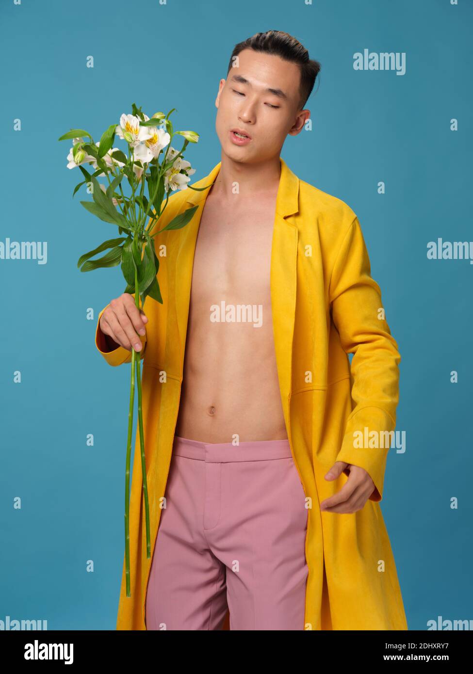 Un uomo in un cappotto giallo e pantaloni rosa tiene un bouquet di fiori  bianchi Foto stock - Alamy