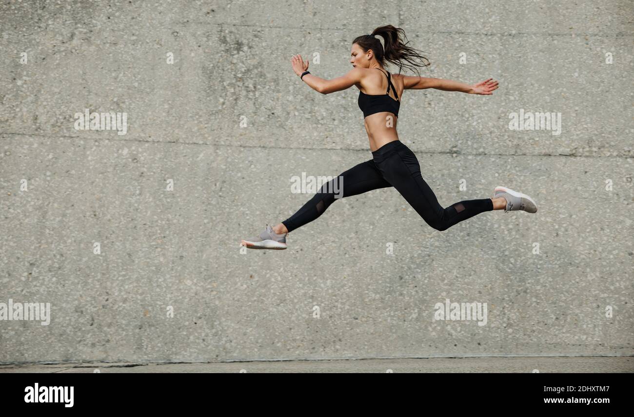 Atleta femminile che corre e salta. Vista laterale dell'atleta flessibile che si esercita all'aperto. Foto Stock