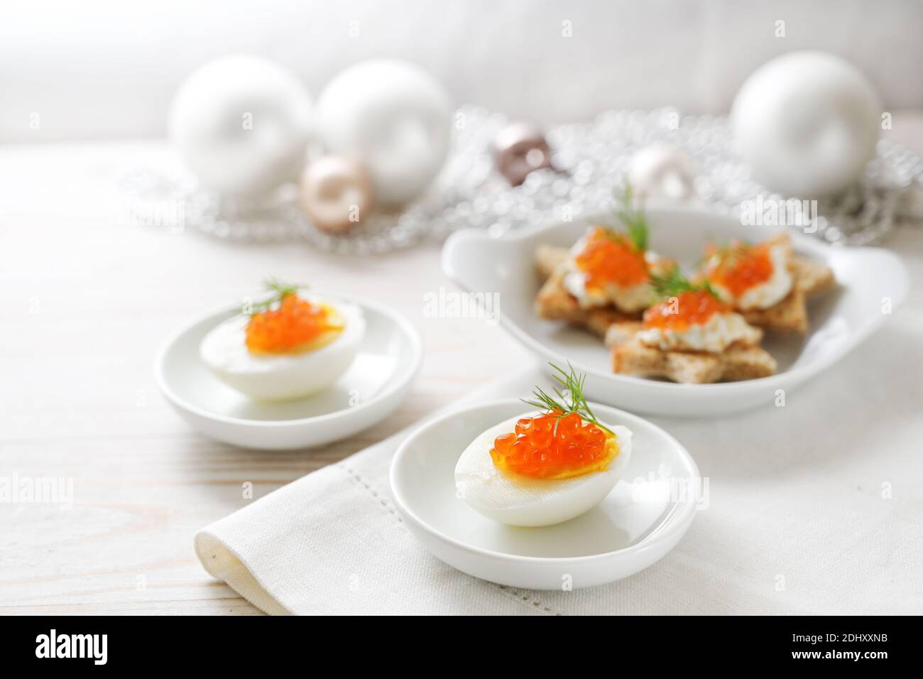 Caviale rosso su uova a metà e tartine a forma di stella, tavolo bianco con decorazione natalizia leggera per un buffet festivo, spazio fotocopie, focu selezionato Foto Stock