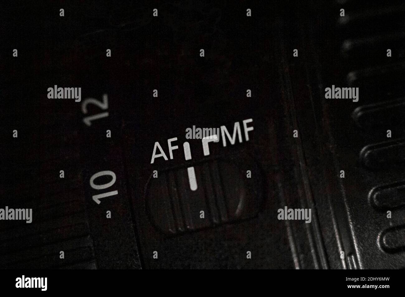 Primo piano dell'interruttore AF MF sull'obiettivo della fotocamera. Cursore per modificare la modalità di messa a fuoco automatica. Sfondo scuro. Foto Stock