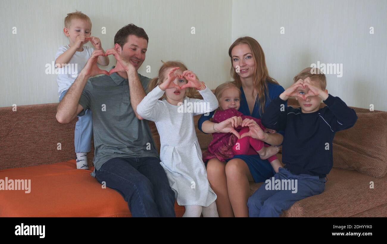 La famiglia grande e amichevole sul divano fa i cuori fuori dalle loro mani. Foto Stock