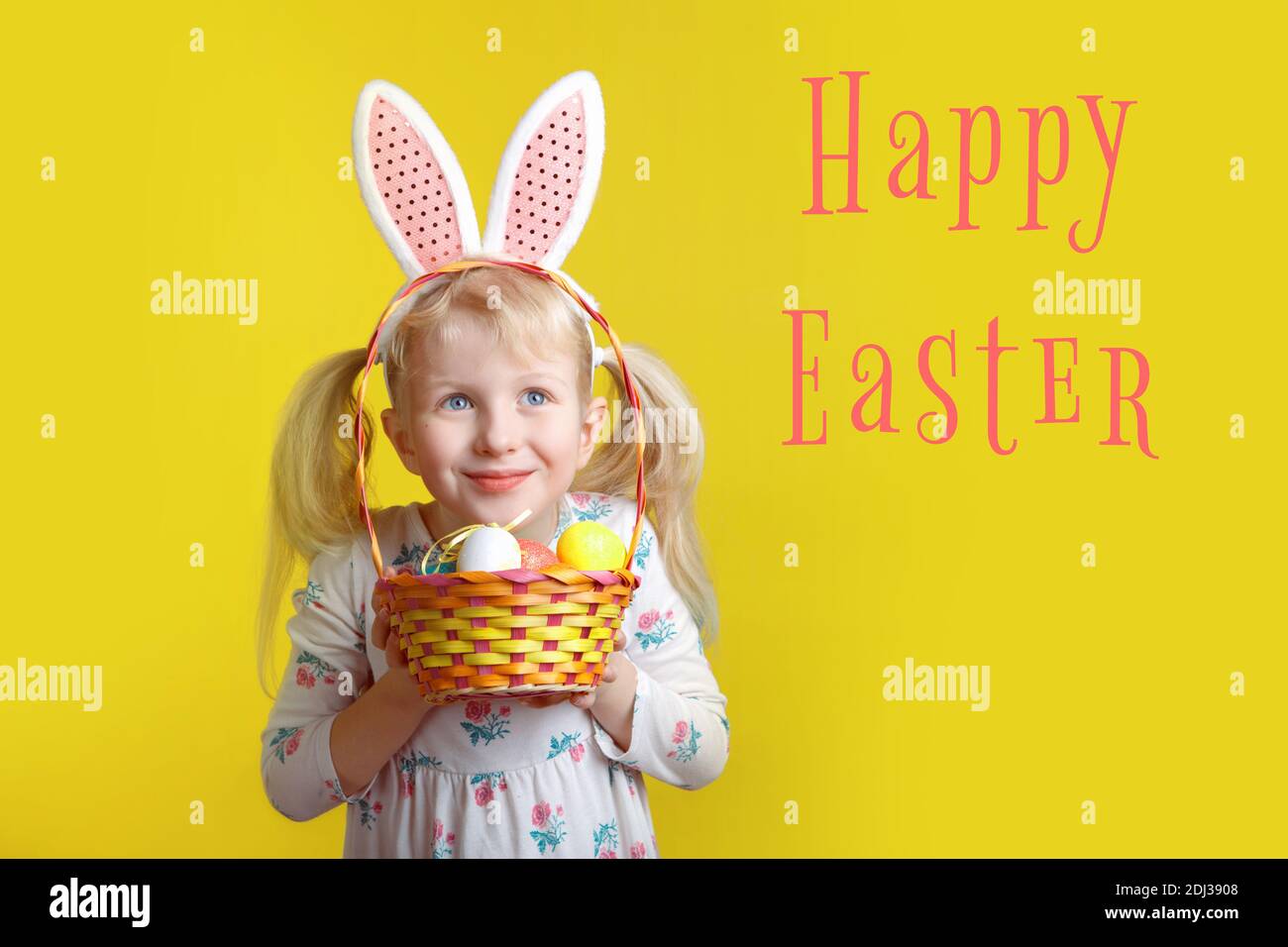 Buona carta pasquale con testo. Caucasica ragazza in rosa Pasqua coniglietto orecchi tenendo cestino con uova. Bambino in studio su sfondo giallo. Capretto divertente c Foto Stock