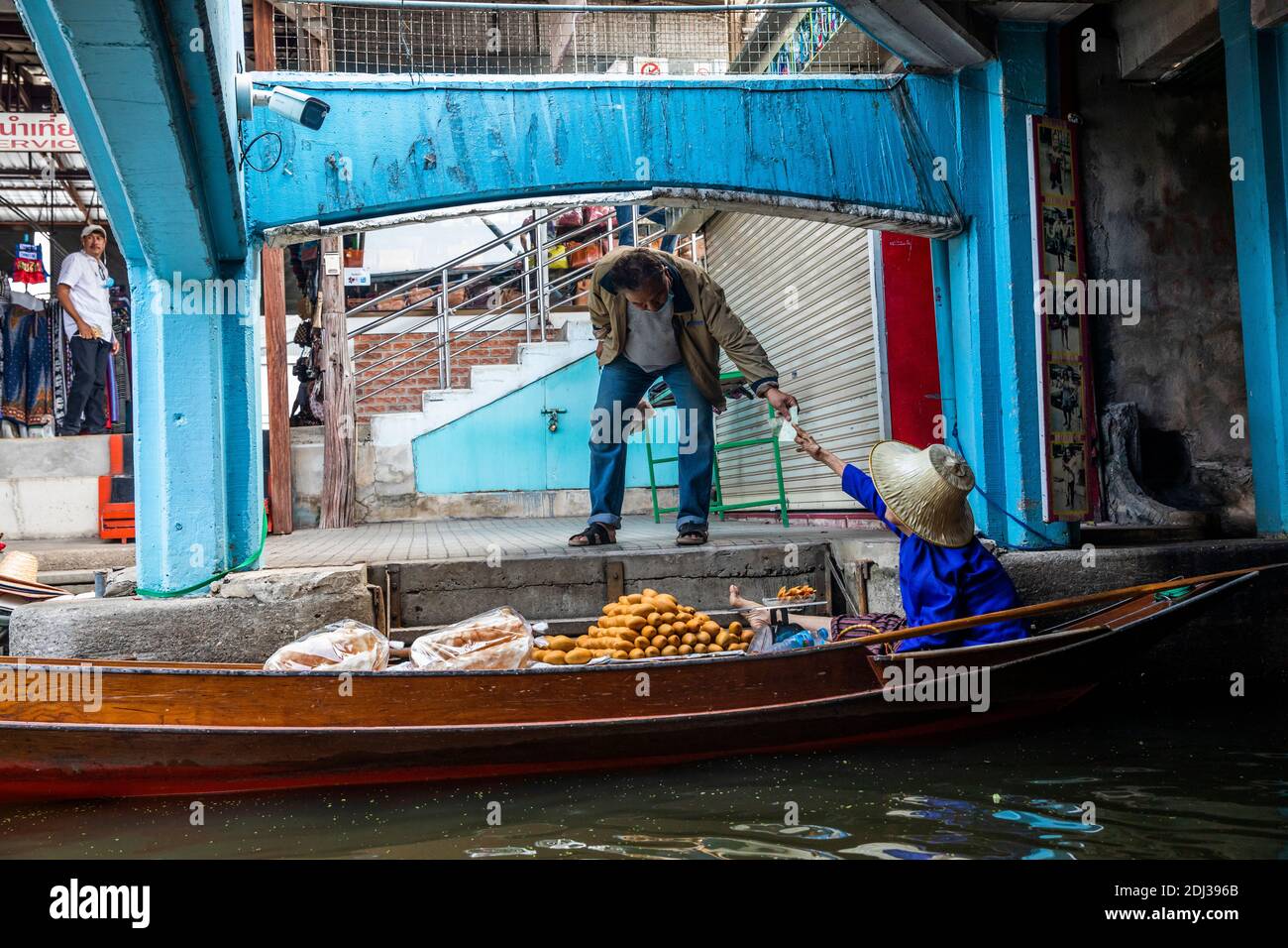 Un uomo thailandese locale raggiunge per fare un acquisto di cibo dal mercante nel mercato galleggiante Damneon vicino Bangkok, Thailandia. Foto Stock