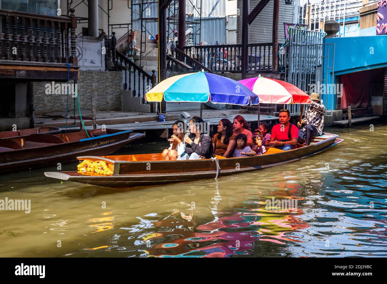 Una donna in una piccola san Pan offre spuntini per la vendita ai turisti in barca più grande con ombrelloni colorati al mercato galleggiante Damneon. Foto Stock Una donna in una piccola san Pan offre spuntini per la vendita ai turisti in barca più grande con ombrelloni colorati al mercato galleggiante Damneon. Foto Stock