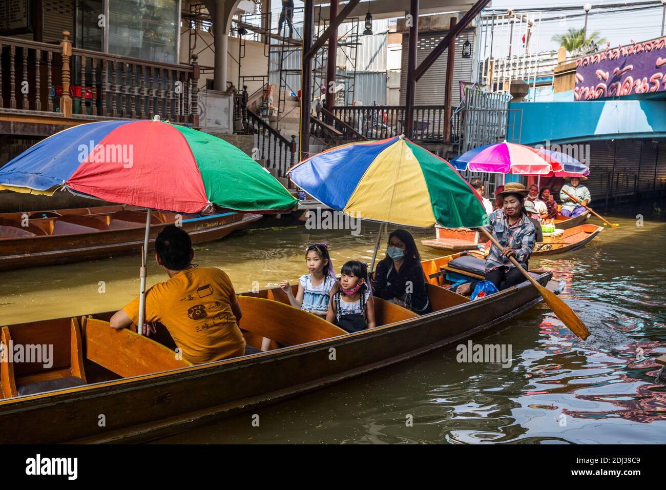 Una donna in una piccola san Pan offre spuntini per la vendita ai turisti in barca più grande con ombrelloni colorati al mercato galleggiante Damneon. Foto Stock Una donna in una piccola san Pan offre spuntini per la vendita ai turisti in barca più grande con ombrelloni colorati al mercato galleggiante Damneon. Foto Stock
