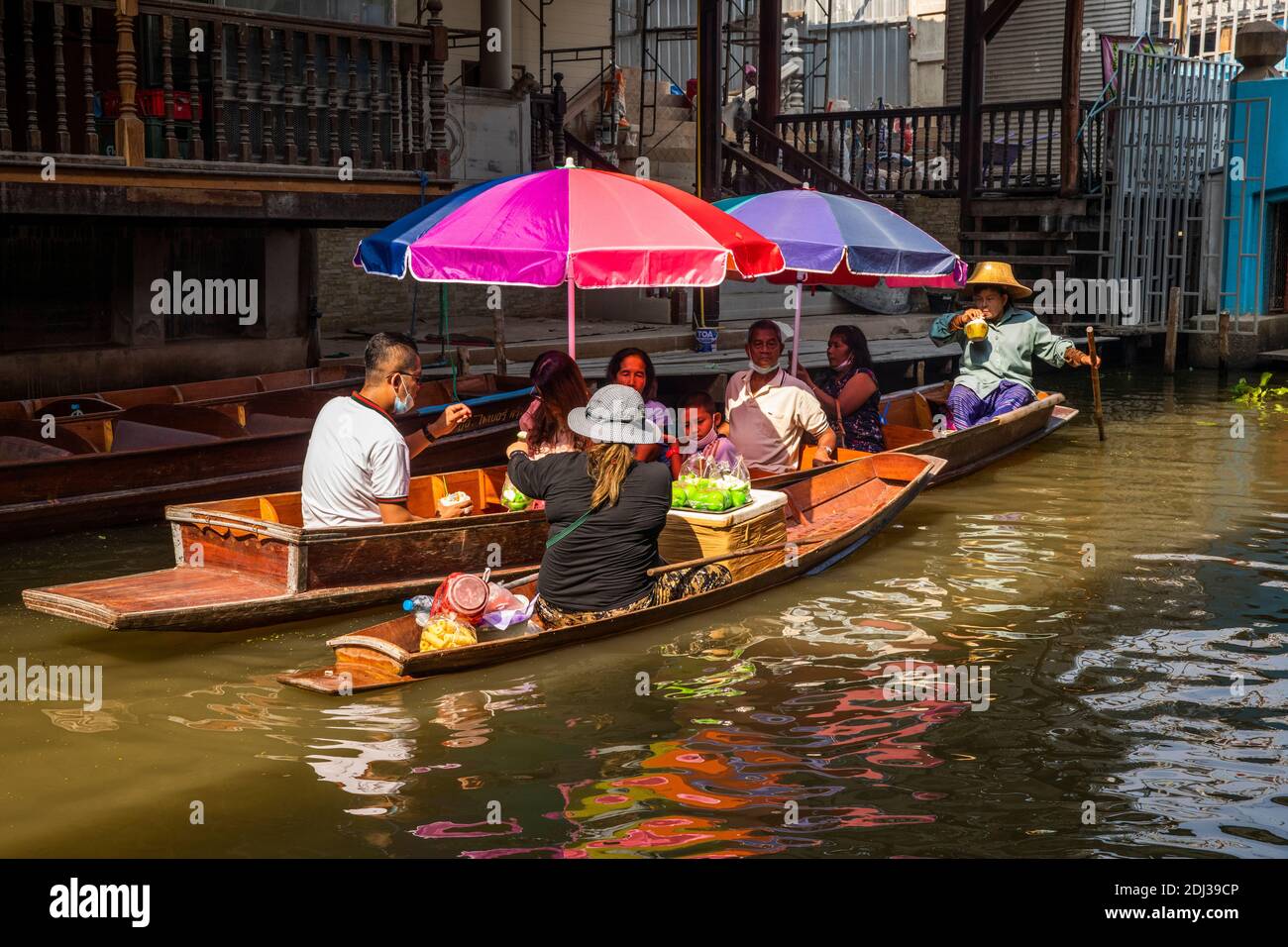 Una donna in una piccola san Pan offre spuntini per la vendita ai turisti in barca più grande con ombrelloni colorati al mercato galleggiante Damneon. Foto Stock Una donna in una piccola san Pan offre spuntini per la vendita ai turisti in barca più grande con ombrelloni colorati al mercato galleggiante Damneon. Foto Stock
