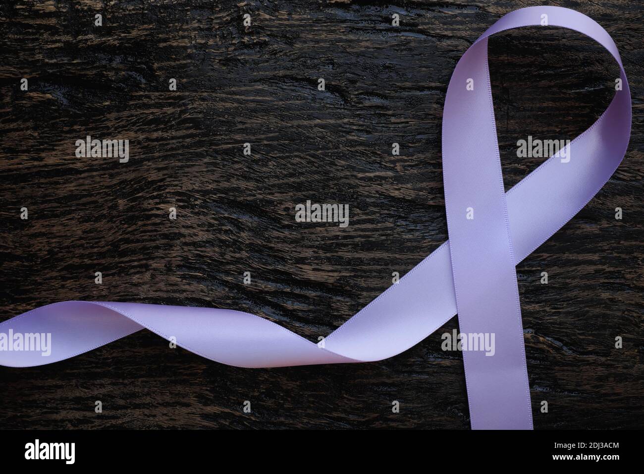 Vista dall'alto del nastro color lavanda o orchidea viola chiaro su sfondo di legno scuro. Cancro generale e testicolare e consapevolezza dell'epilessia Foto Stock