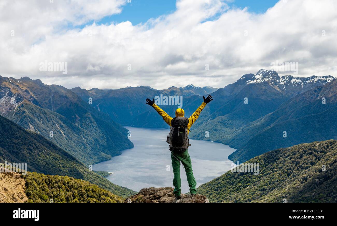 Alpinista, escursionista guarda in lontananza, allungando le braccia in aria, vista del fiordo sud del lago te Anau, Murchison Montagne e del sud Foto Stock