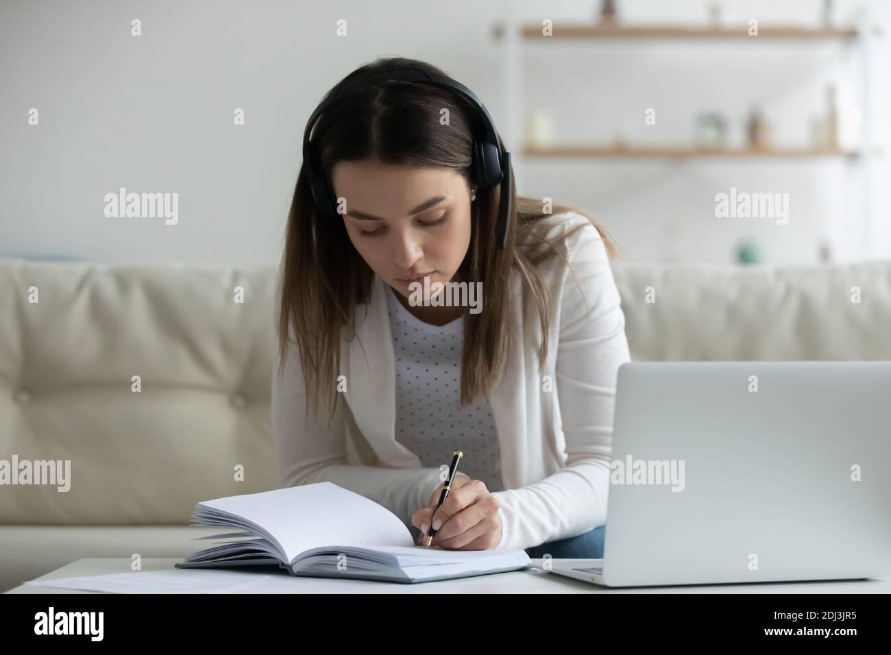 Donna giovane e mirata che indossa le cuffie con il computer portatile, scrivendo note Foto Stock