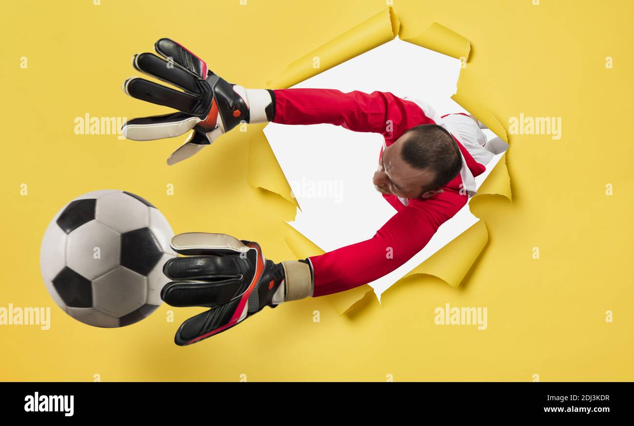 Il portiere esce da un buco e cerca di tatches la palla. Sfondo giallo Foto Stock