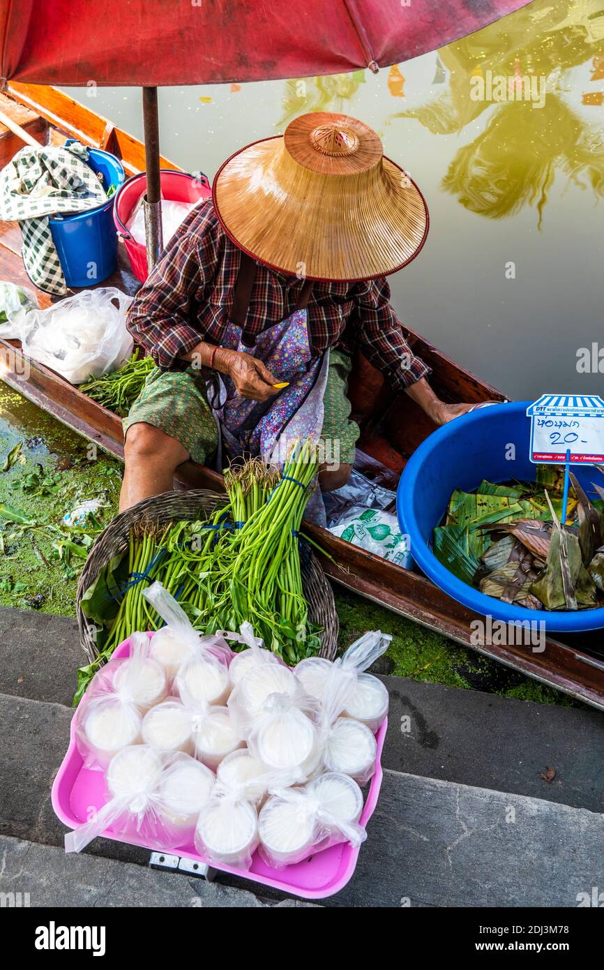 Una donna protetta dal suo cappello thailandese e ombrello lavora sulla sua san Pan da cui vende prodotti e riso. Foto Stock