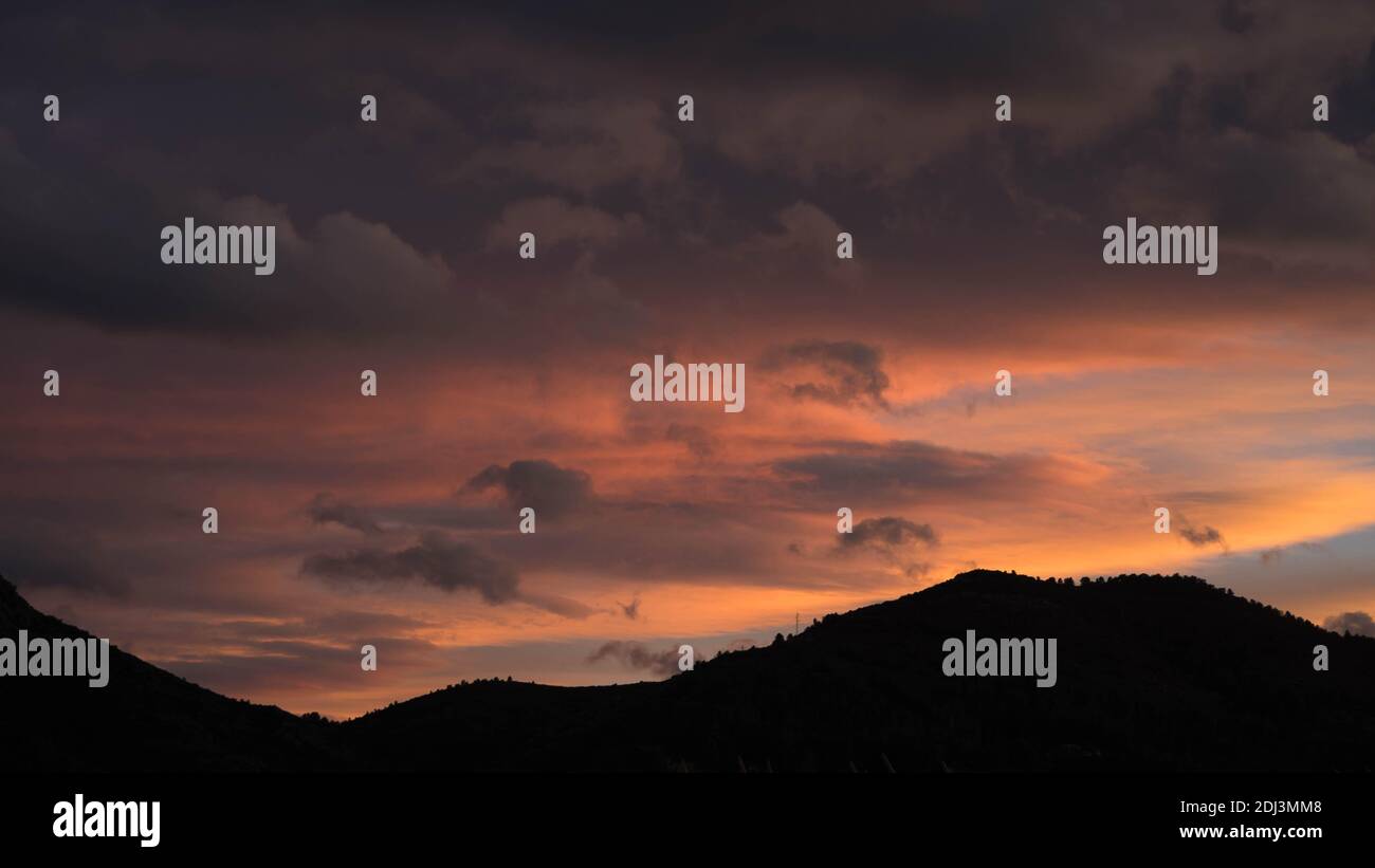 Nuvole al tramonto morbide e colorate su colline scure Foto Stock