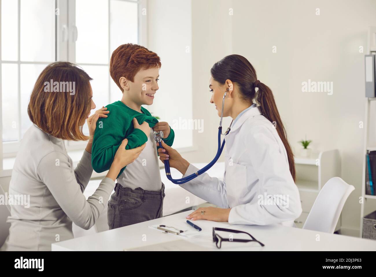 Il medico ascolta con uno stetoscopio un ragazzo che è venuto con la madre per un esame medico. Foto Stock