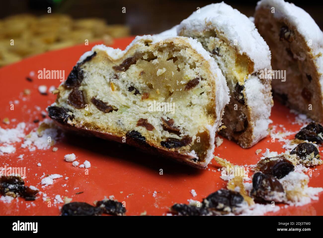 Primo piano di christstollen affettato con uvetta, zucchero bianco in polvere e marzapane su piatto rosso Foto Stock