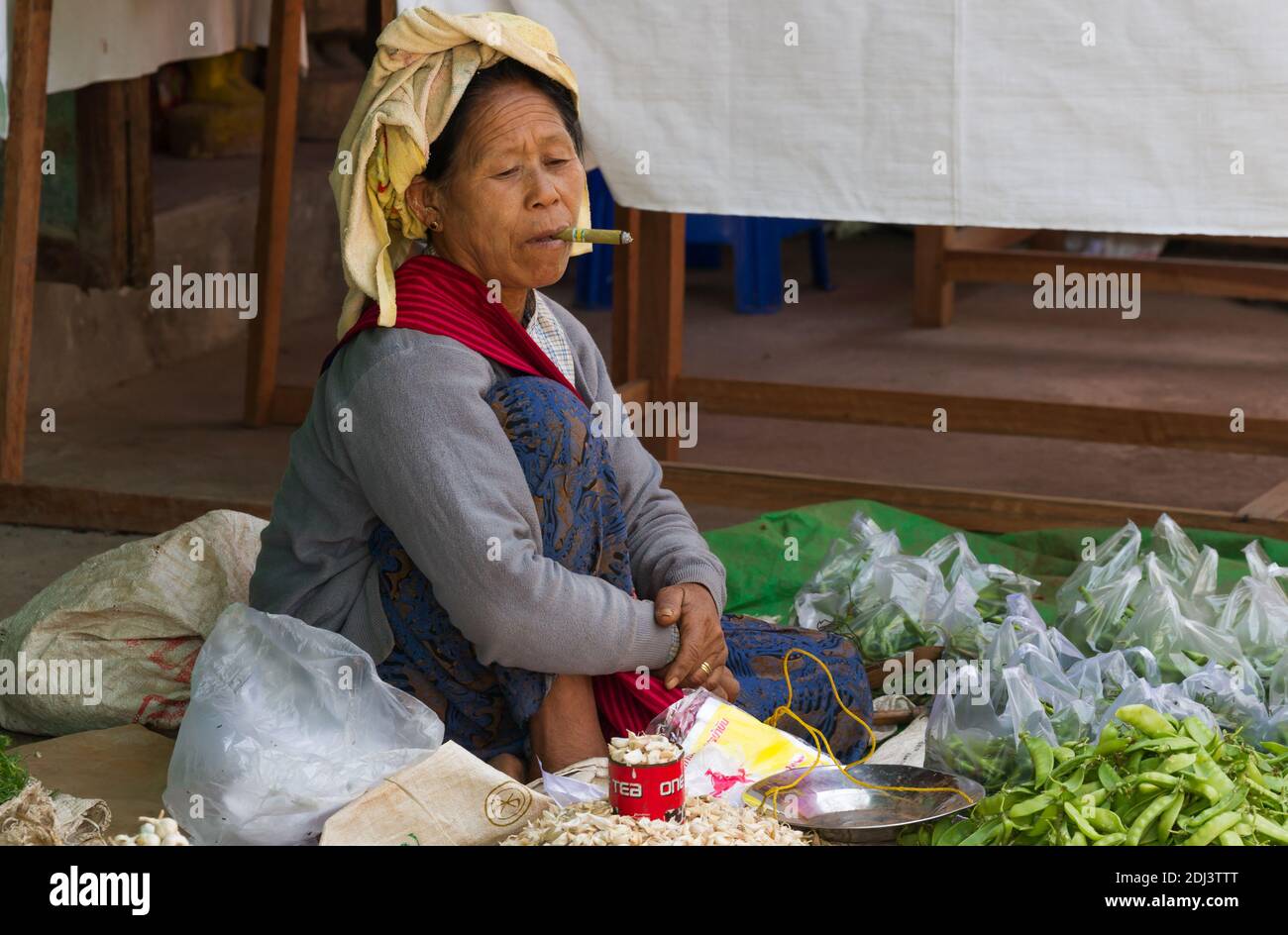 Nyaung Shwe, Myanmar - 24 novembre 2014: Donna che vende verdure al mercato locale fuma un sigaro mentre attende i clienti. Foto Stock