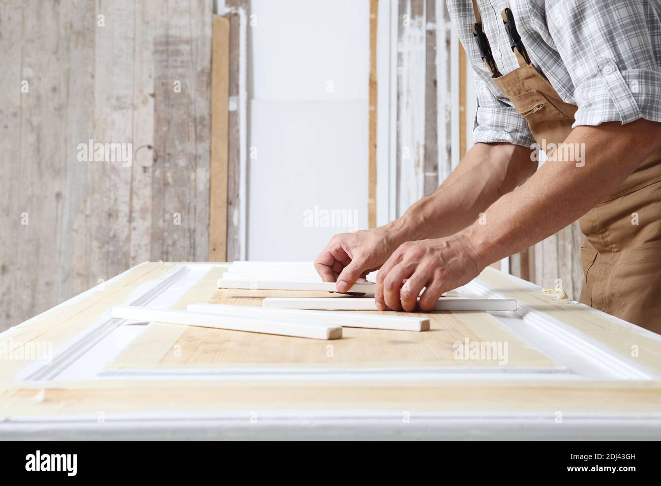 Falegname maschile che lavora il legno in officina di Falegnameria, mettendo bastoni di legno su una porta, indossare tuta Foto Stock