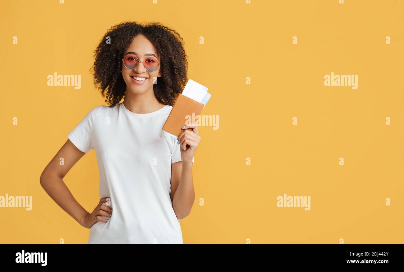 Felice giovane donna afroamericana con capelli ricci tiene il passaporto con biglietti aerei Foto Stock