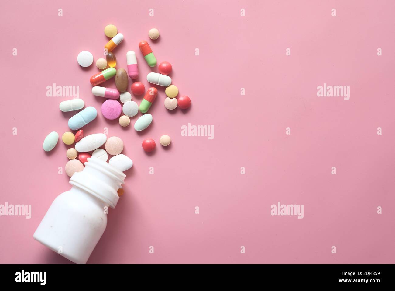 primo piano di pillole colorate e capsula versando sul rosa Foto Stock