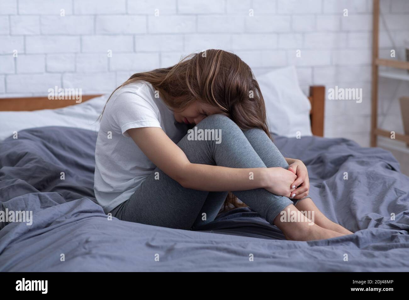 Infelice giovane donna che soffre di depressione, nascondendo il viso e piangendo a letto a casa Foto Stock