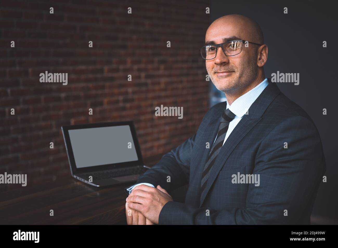 Uomo d'affari calvo maturo in occhiali che lavorano da solo al suo scrivania in ufficio fino a tarda notte seduta a metà strada con schermo bianco su computer portatile e. Foto Stock