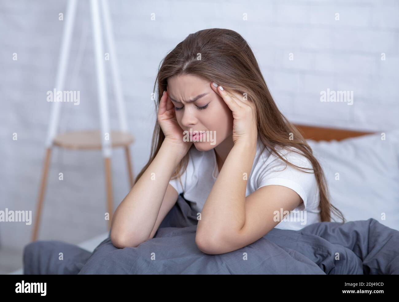 Depressa giovane donna massaggiando i suoi templi per alleviare mal di testa o. stress a letto Foto Stock