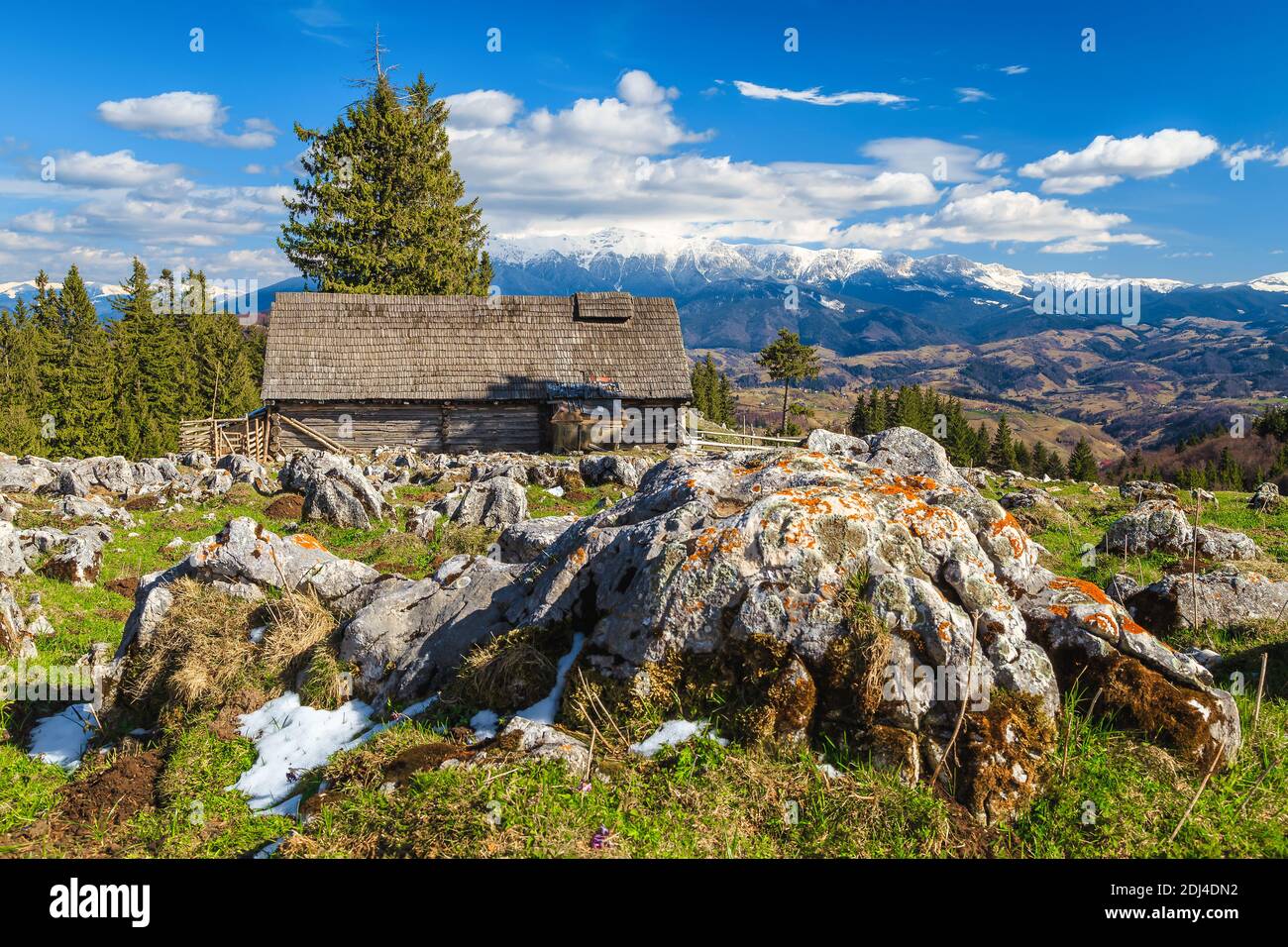 Pittoresco paesaggio rurale di primavera con vecchia capanna di legno e alte montagne innevate sullo sfondo, Transilvania, Romania, Europa Foto Stock