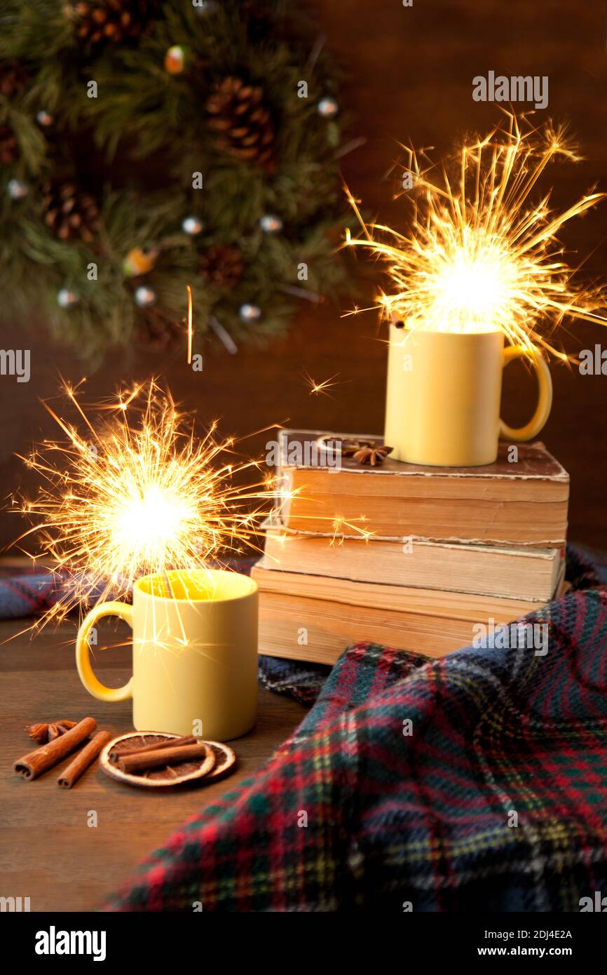 tazze da tè con sfondo brillante e natalizio, tazza in ceramica con luce brillante all'interno, libri e coperta con rotoli e cannella Foto Stock