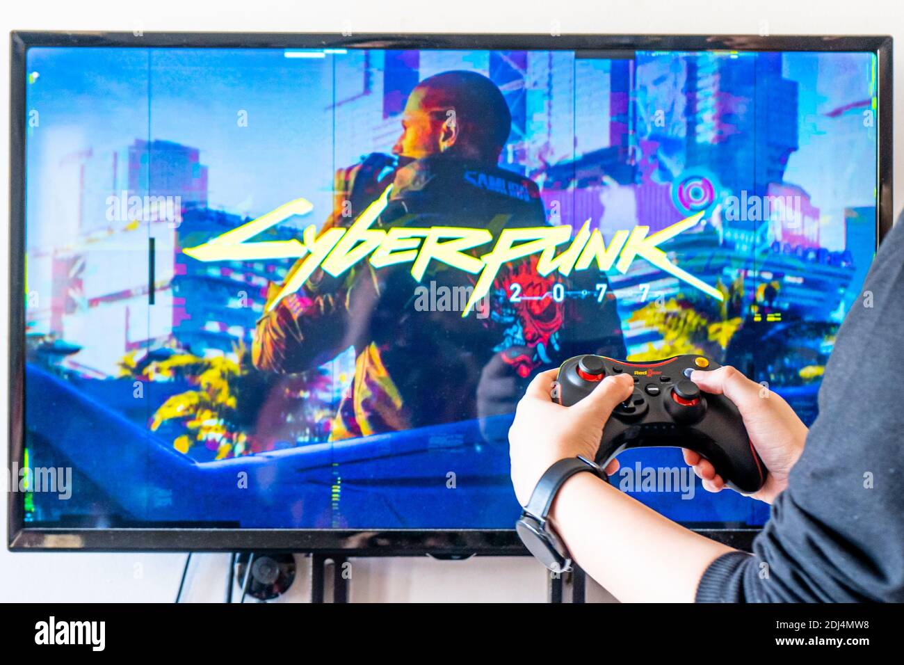 Donna che tiene un controller Red Gear e riproduce video popolari Gioco Cyberpunk 2077 su un televisore e PC Foto Stock