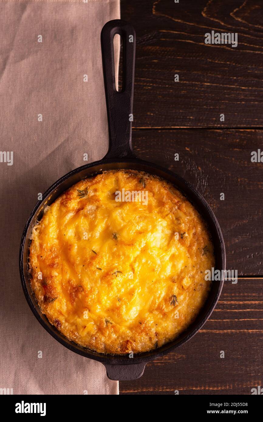 Frittata con formaggio, mozzarella e zucca stufata in una padella di ghisa su sfondo ligneo Foto Stock