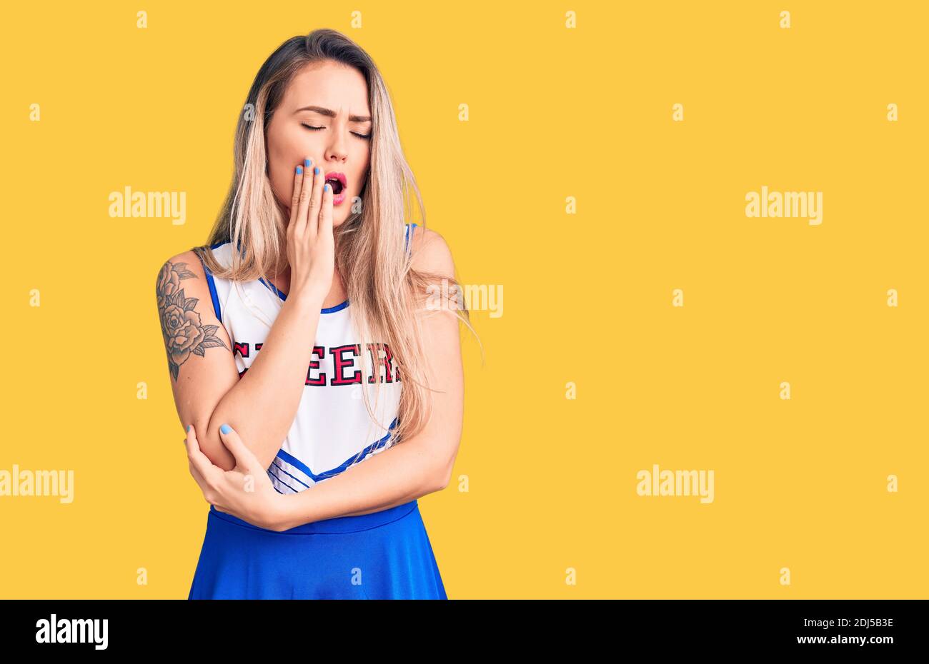 Giovane bella donna bionda che indossa cheerleader uniforme annoiato yawning stanco coprire la bocca con la mano. Inquietante e sonnolenza. Foto Stock