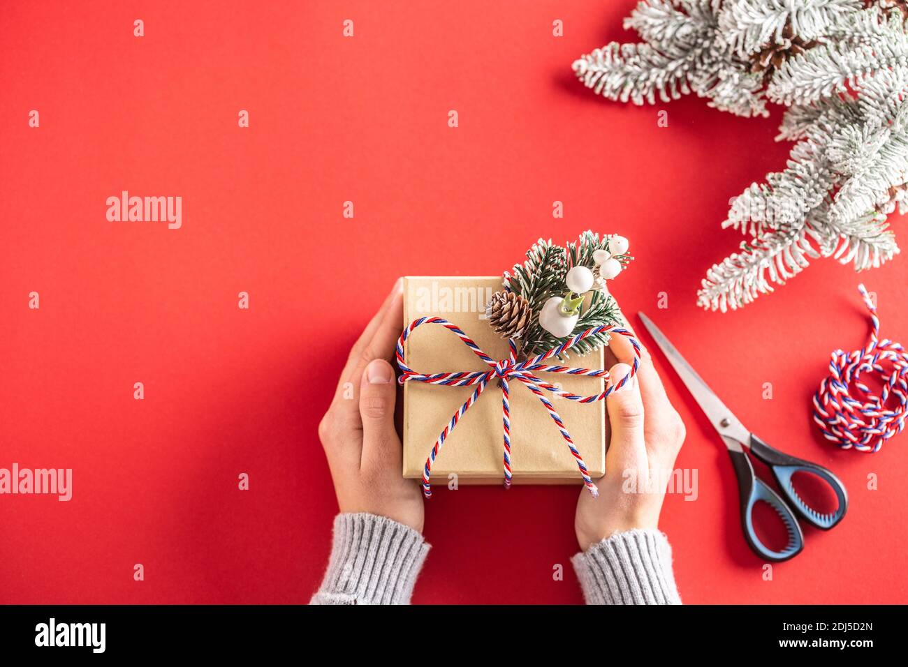Regalo di Natale imballando in una carta eco-friendly con forbici, spago, e ramificazione di albero di conifere a sfondo rosso. Foto Stock