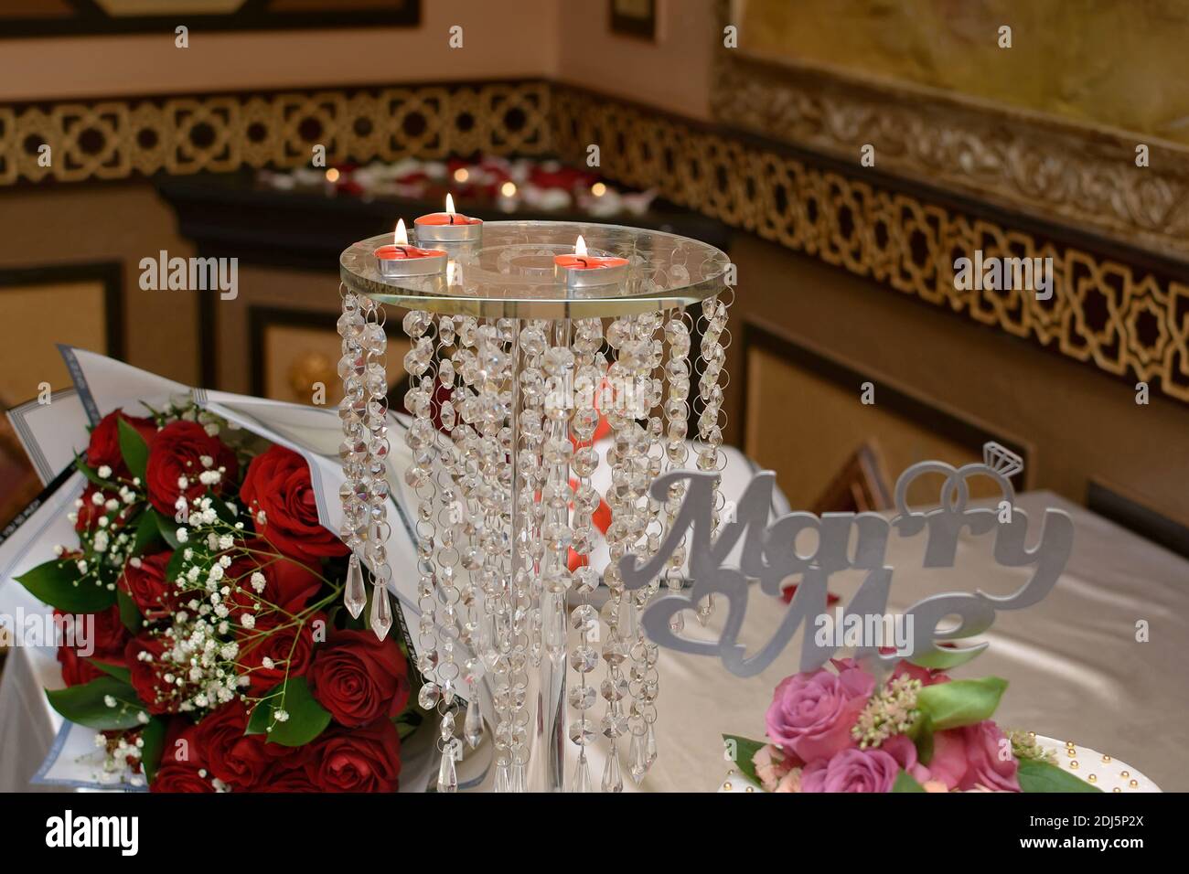 Candele accese sotto forma di cuori su un tavolo di vetro in un ristorante, accanto ad un bouquet di fiori e l'iscrizione sulla torta 'Marry Me' Foto Stock