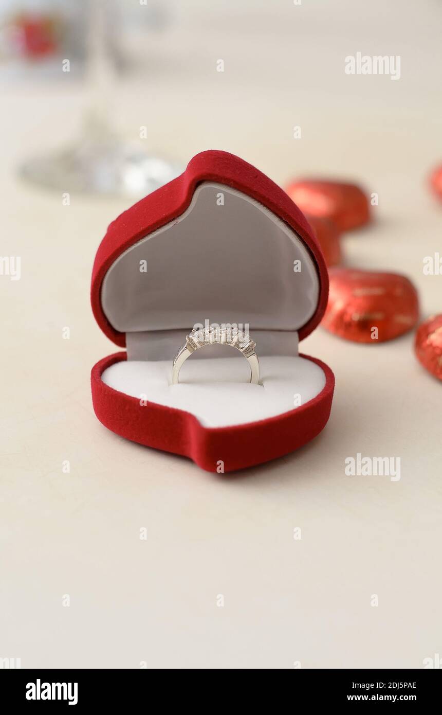 Anello in argento in una scatola rossa a forma di cuore, su un tavolo bianco su sfondo di dolci Foto Stock