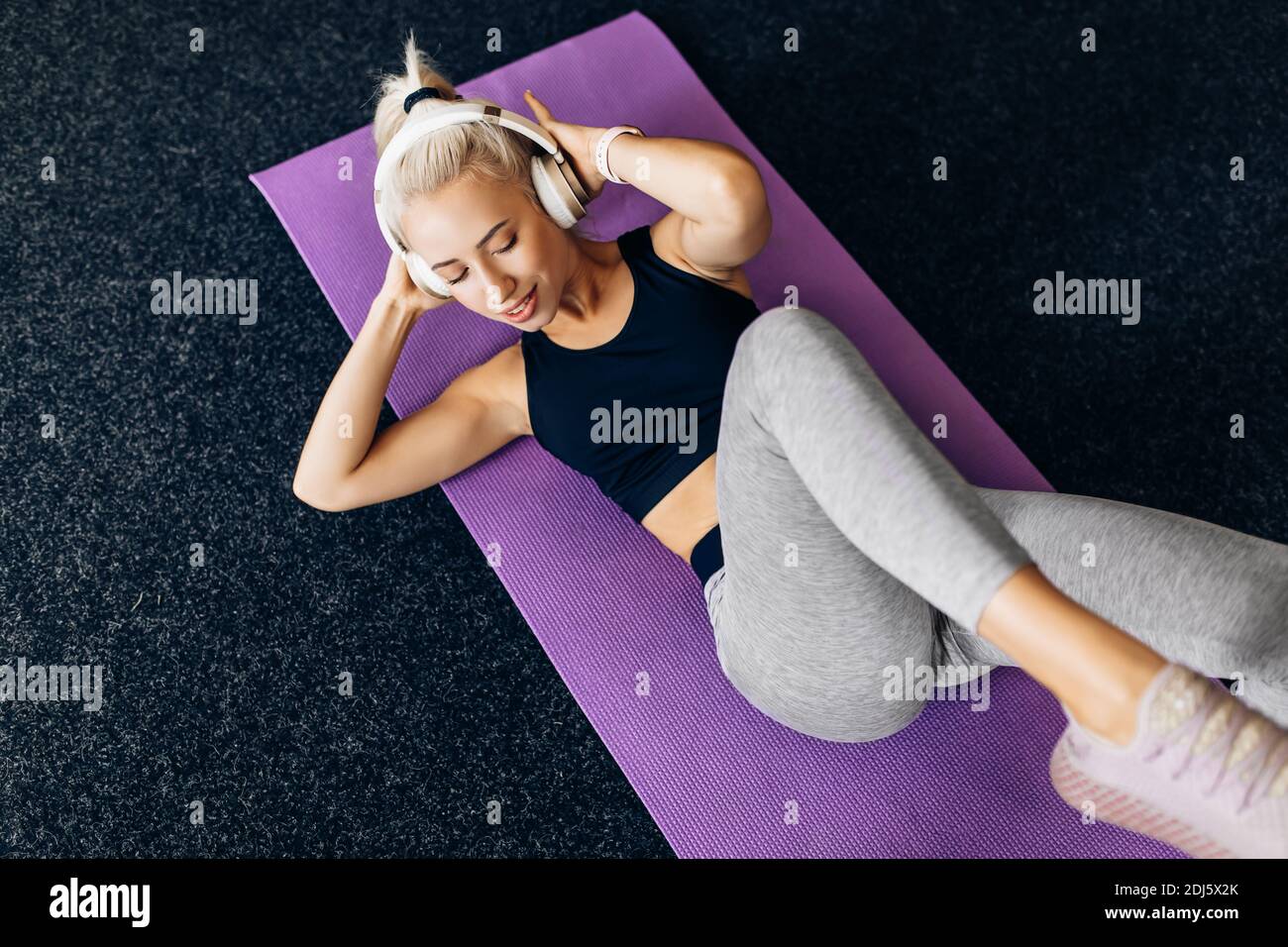 giovane donna che ascolta la musica con le cuffie che fanno esercizi di ab sul tappetino fitness in palestra Foto Stock